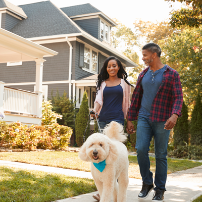 Happy couple walking their dog in front of their newly mortgaged home, representing homeownership with St. Mary’s Bank mortgage services