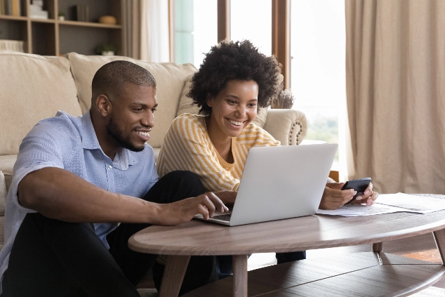 Couple sitting on the floor planning their finances on a laptop while managing accounts with St. Mary’s Bank