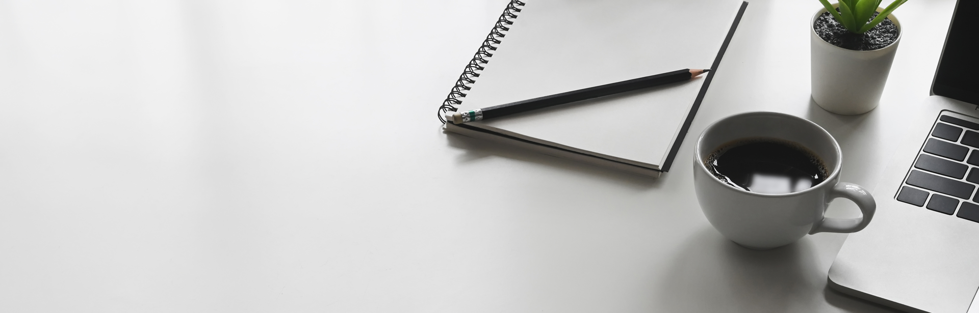White table with laptop, cup of coffee, and notebook with pen laying on top