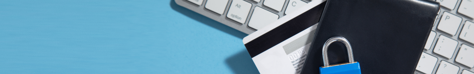 A keyboard, credit card, and wallet laying on a blue background with a padlock laying on them