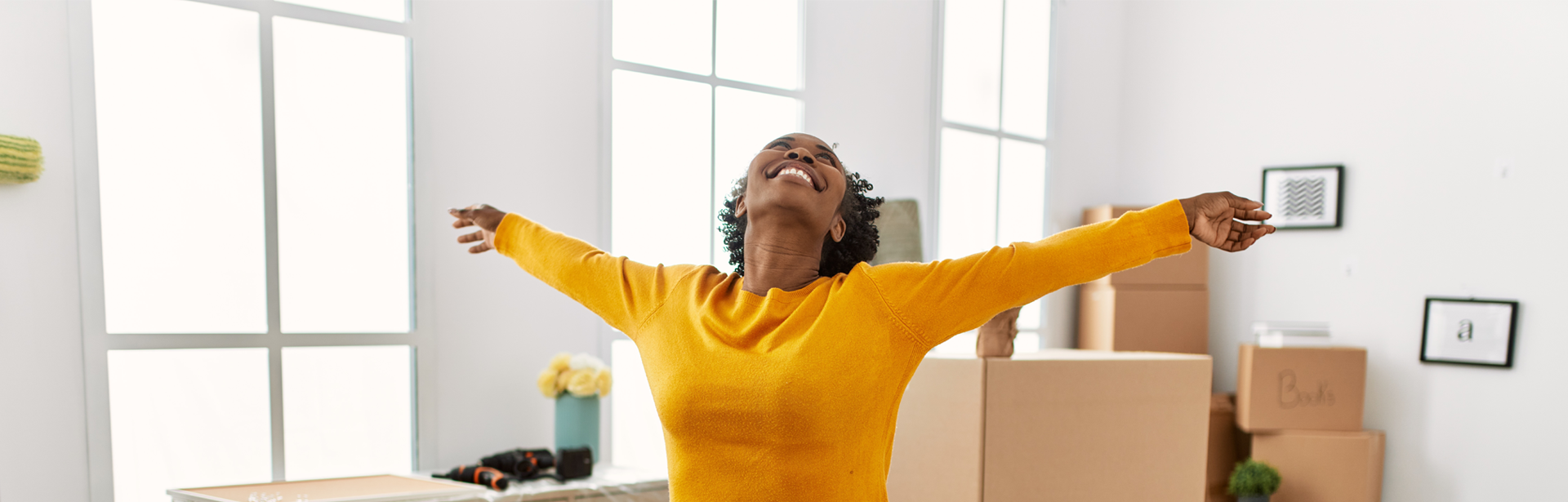 Woman unpacking boxes in a home stretches her arms out in celebration
