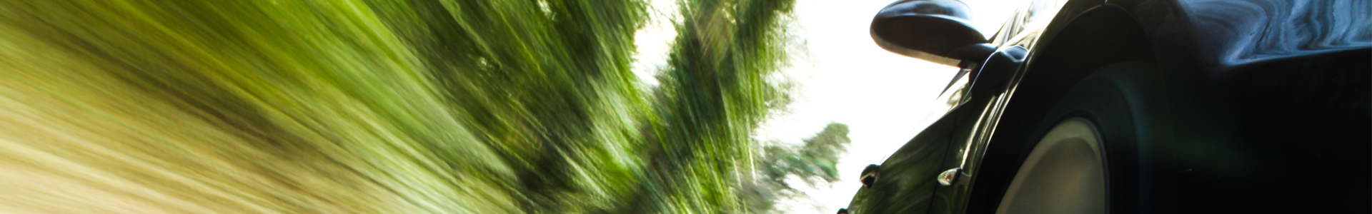 Black car traveling at high speeds with blurred green foliage in the background